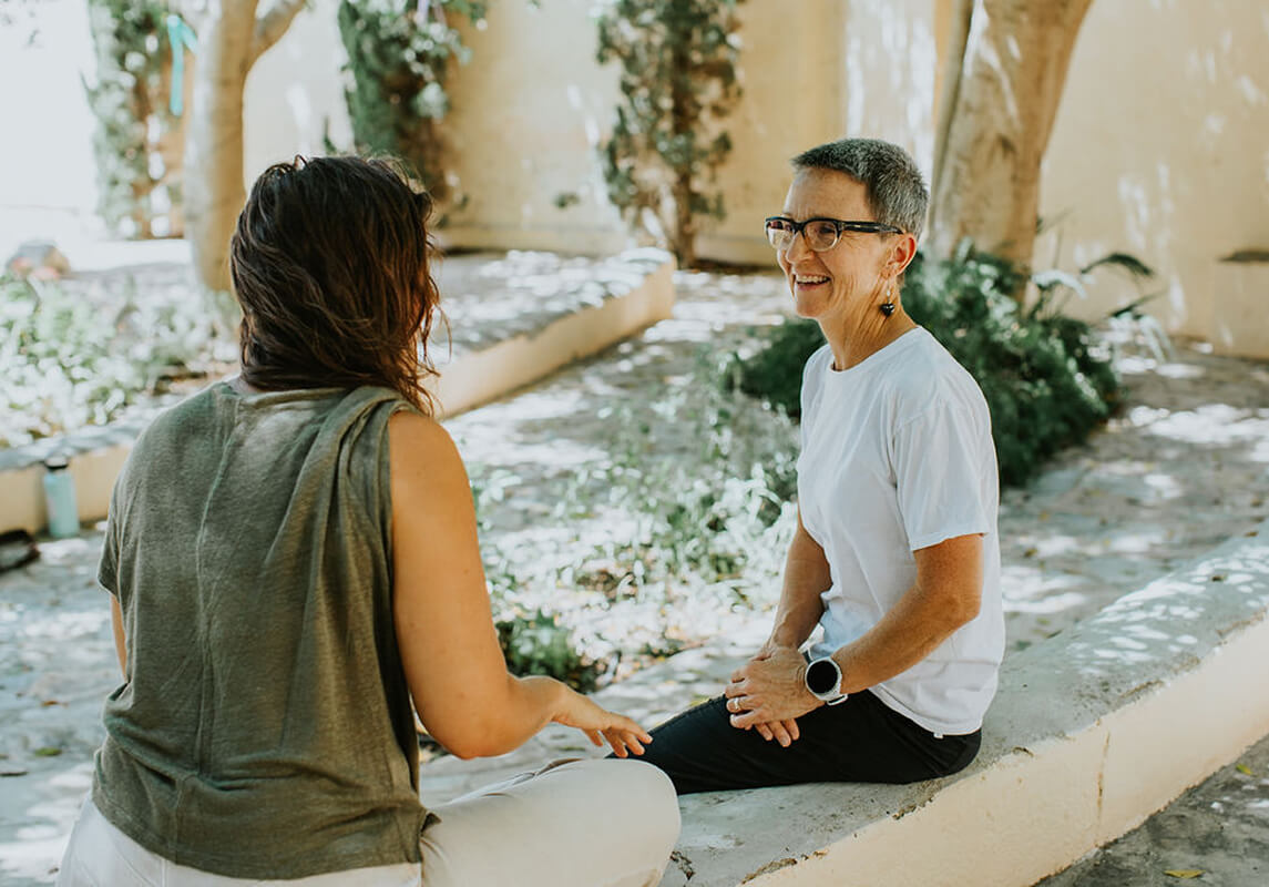 Two women talking together in a shaded courtyard